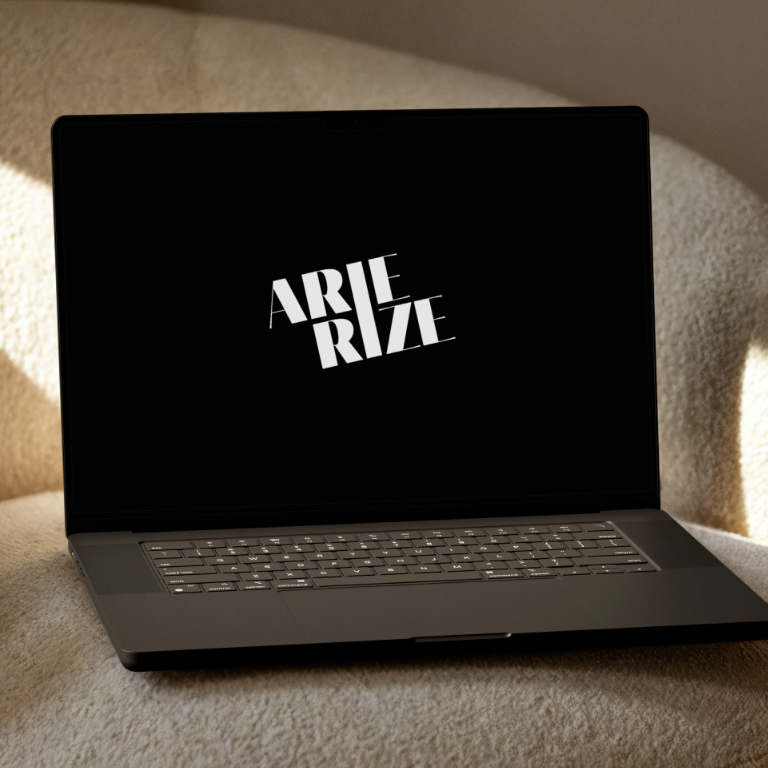Ein MacBook auf einem Sessel. Das Display zeigt das Logo von Arie Rize auf schwarzem Hintergrund.